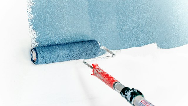 Paint roller applying smooth coating to interior wall drywall surface